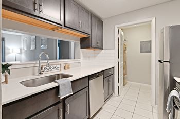 A kitchen with stainless steel appliances and white countertops and a door to a hallway